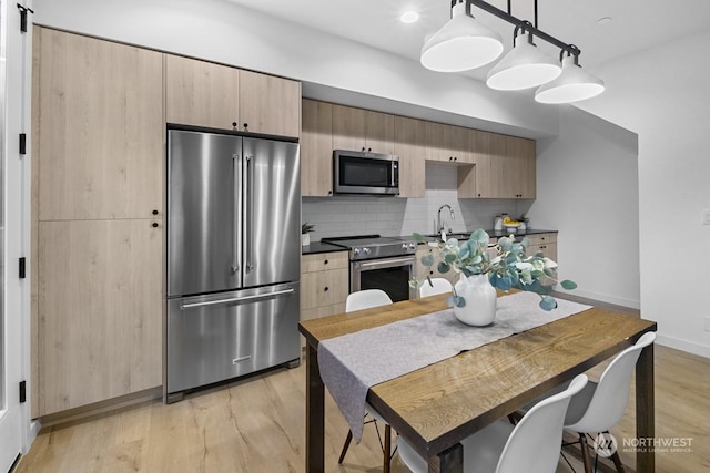 kitchen with light hardwood / wood-style floors, appliances with stainless steel finishes, tasteful backsplash, hanging light fixtures, and light brown cabinets