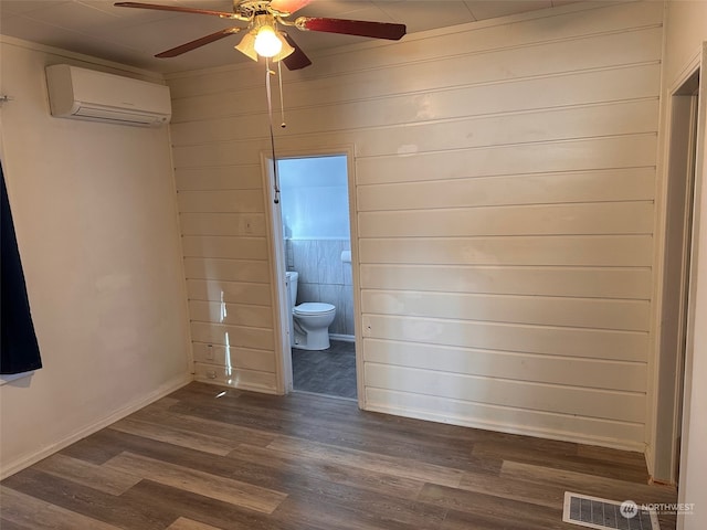 unfurnished bedroom with ceiling fan, wooden walls, ensuite bathroom, a wall mounted air conditioner, and dark hardwood / wood-style flooring