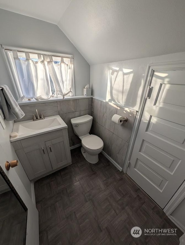bathroom with vaulted ceiling, tile walls, parquet floors, vanity, and toilet
