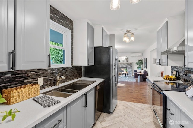 kitchen with black appliances, light parquet flooring, tasteful backsplash, sink, and a wall mounted AC