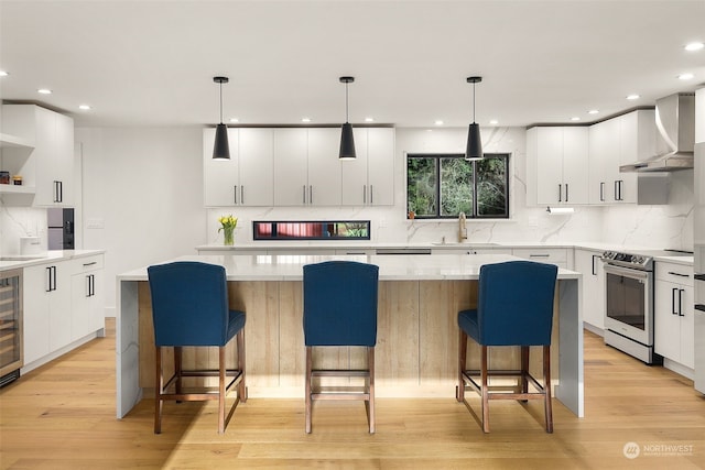 kitchen featuring wall chimney range hood, a kitchen island, a breakfast bar, sink, and stainless steel range with electric cooktop