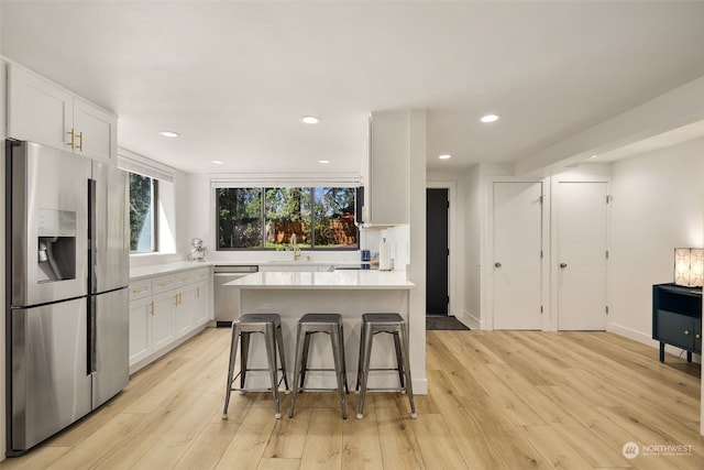 kitchen featuring appliances with stainless steel finishes, light wood-type flooring, a kitchen island, white cabinets, and a breakfast bar