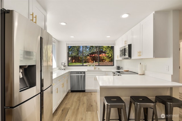 kitchen with white cabinets, stainless steel appliances, sink, light wood-type flooring, and a breakfast bar