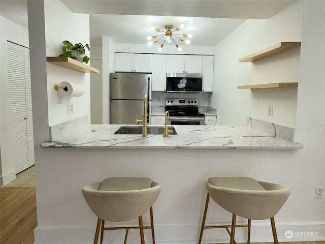 kitchen featuring white cabinets, appliances with stainless steel finishes, a kitchen bar, kitchen peninsula, and light stone counters