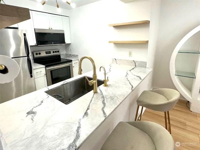 kitchen featuring light stone countertops, appliances with stainless steel finishes, white cabinetry, sink, and light hardwood / wood-style flooring