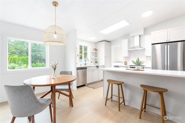 kitchen with pendant lighting, white cabinetry, light hardwood / wood-style flooring, appliances with stainless steel finishes, and wall chimney exhaust hood