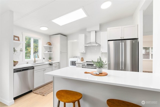 kitchen with white cabinets, appliances with stainless steel finishes, wall chimney exhaust hood, a kitchen bar, and sink