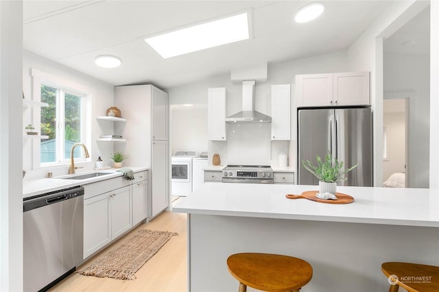 kitchen with washer and dryer, wall chimney exhaust hood, stainless steel appliances, sink, and a kitchen breakfast bar