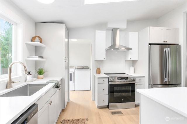 kitchen featuring wall chimney range hood, sink, washing machine and clothes dryer, stainless steel appliances, and white cabinets