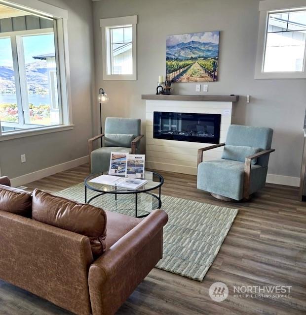 living area with dark wood-style flooring, a glass covered fireplace, and baseboards