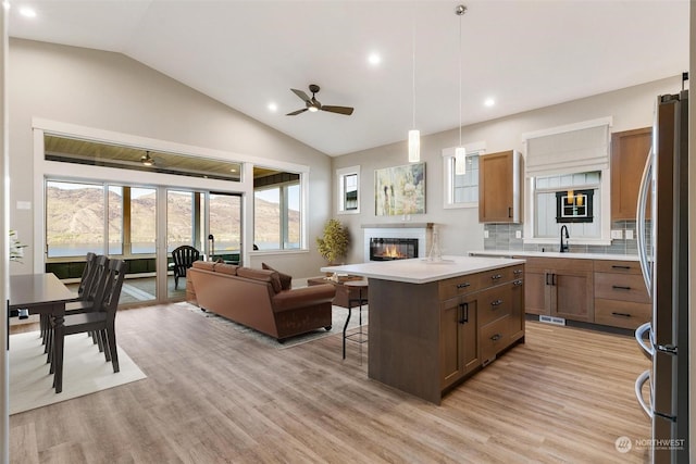 kitchen with open floor plan, light countertops, freestanding refrigerator, a center island, and a glass covered fireplace