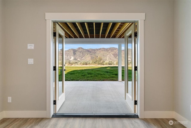 doorway with light wood-style flooring, a mountain view, and baseboards