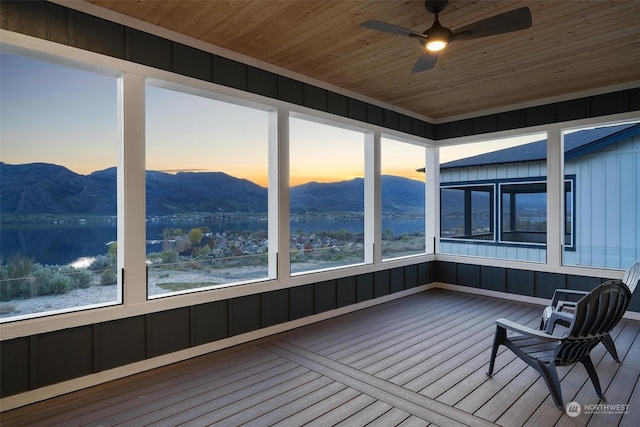 unfurnished sunroom featuring wood ceiling, ceiling fan, plenty of natural light, and a mountain view