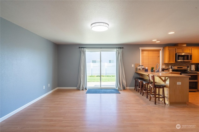 kitchen with sink, light hardwood / wood-style flooring, kitchen peninsula, stainless steel appliances, and a breakfast bar area