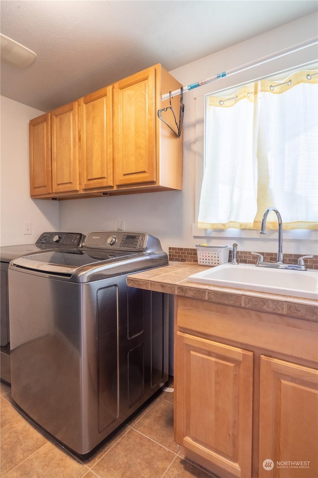 clothes washing area with sink, light tile patterned flooring, cabinets, and washing machine and clothes dryer