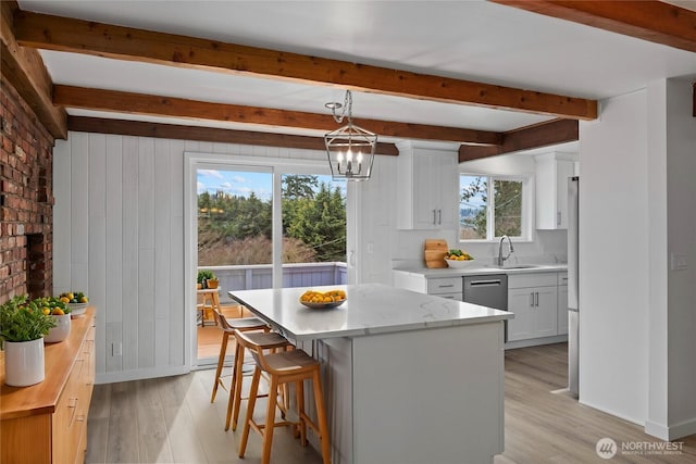 kitchen with light wood finished floors, white cabinets, stainless steel dishwasher, beamed ceiling, and a center island