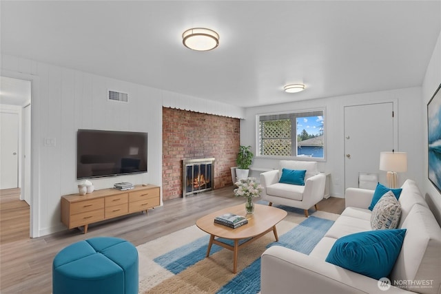 living area with visible vents, a brick fireplace, and light wood-style floors