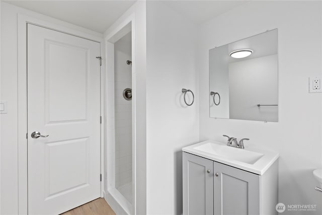 bathroom featuring toilet, tiled shower, vanity, and wood finished floors