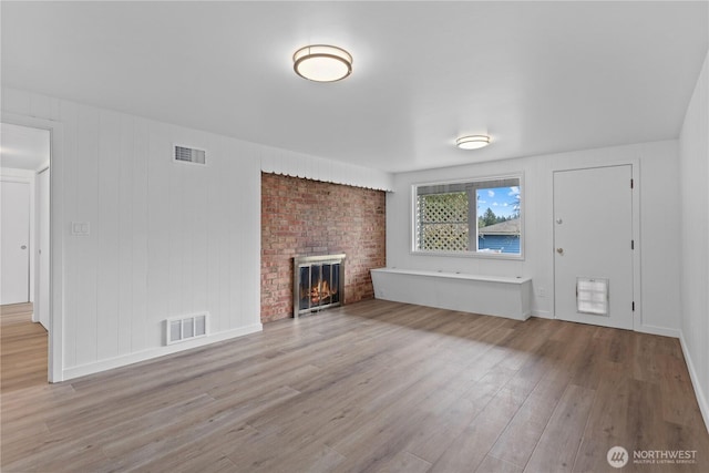 unfurnished living room with wood finished floors, a fireplace, visible vents, and baseboards