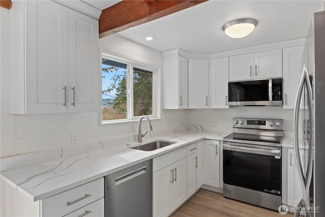 kitchen featuring a sink, light stone counters, appliances with stainless steel finishes, and white cabinetry