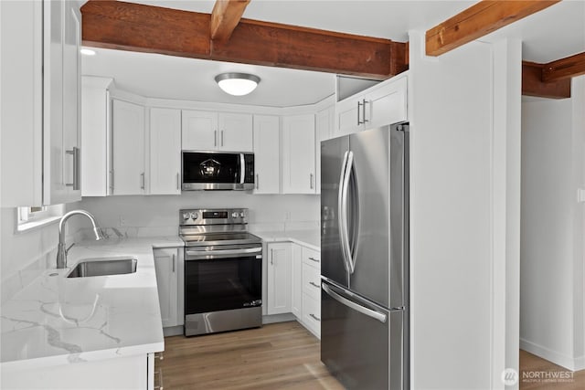 kitchen with beam ceiling, light stone counters, appliances with stainless steel finishes, white cabinetry, and a sink