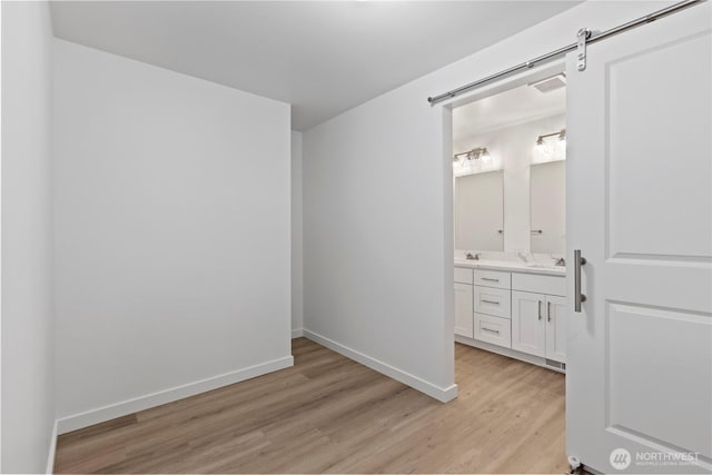 interior space with visible vents, baseboards, a barn door, light wood-style floors, and ensuite bath