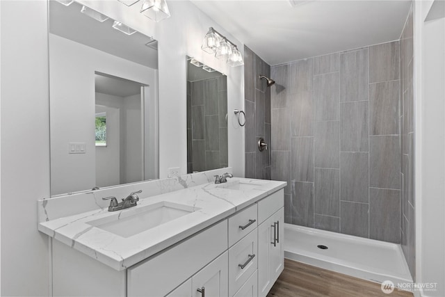 bathroom featuring double vanity, a tile shower, and a sink