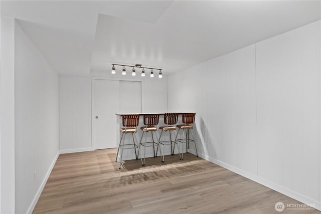 unfurnished dining area featuring baseboards, a bar, wood finished floors, and track lighting