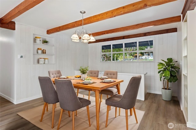 dining area with beam ceiling, a notable chandelier, wood finished floors, and baseboards