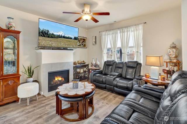 living room featuring light hardwood / wood-style floors, a tile fireplace, and ceiling fan