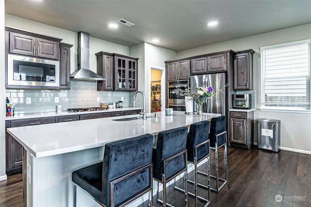 kitchen with a breakfast bar, sink, wall chimney exhaust hood, and stainless steel appliances