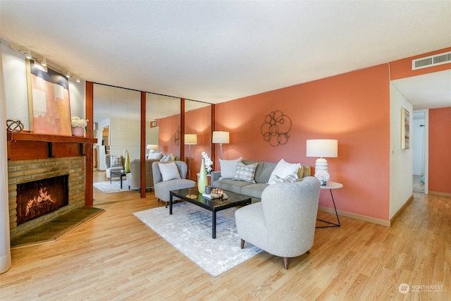 living room featuring light hardwood / wood-style floors, a textured ceiling, and a brick fireplace