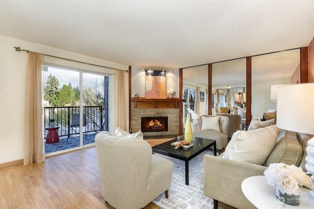 living room with a brick fireplace, a textured ceiling, and light wood-type flooring