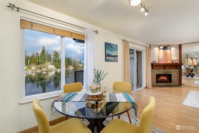 dining room featuring a water view, a brick fireplace, light hardwood / wood-style flooring, and a textured ceiling