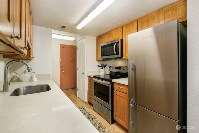 kitchen featuring sink, stainless steel appliances, light wood-type flooring, and a textured ceiling