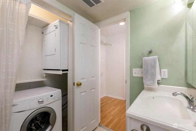 washroom featuring sink, light wood-type flooring, and stacked washing maching and dryer