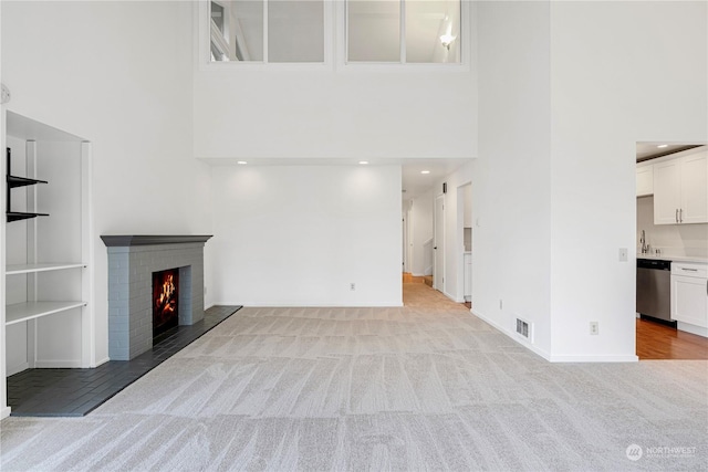 unfurnished living room with a brick fireplace, sink, light carpet, and a towering ceiling