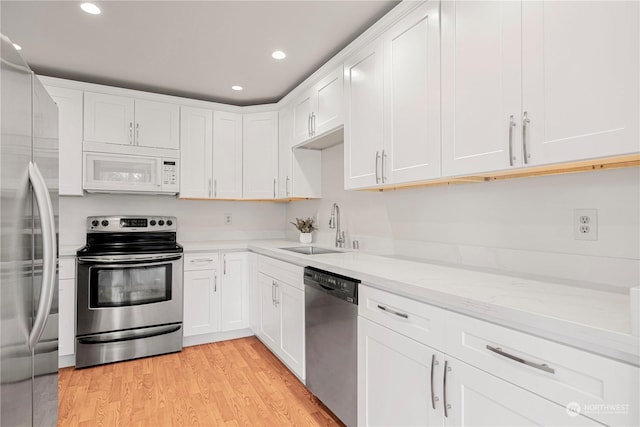 kitchen featuring light hardwood / wood-style floors, appliances with stainless steel finishes, sink, white cabinets, and light stone counters