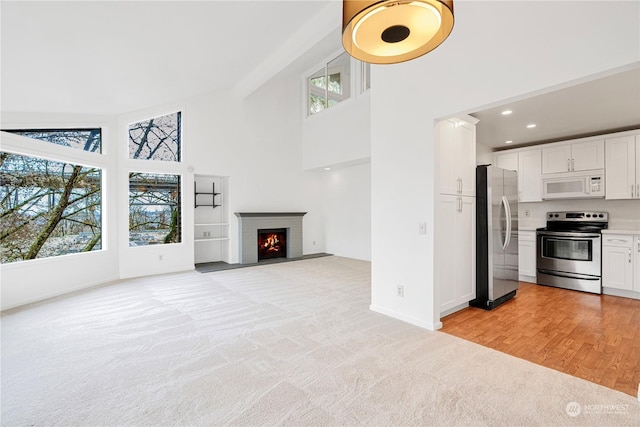 unfurnished living room with a brick fireplace, high vaulted ceiling, and light wood-type flooring