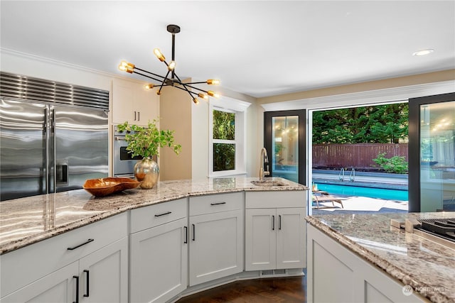 kitchen featuring light stone countertops, appliances with stainless steel finishes, white cabinetry, sink, and decorative light fixtures