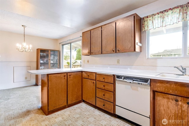 kitchen with dishwasher, light countertops, a peninsula, brown cabinetry, and a sink