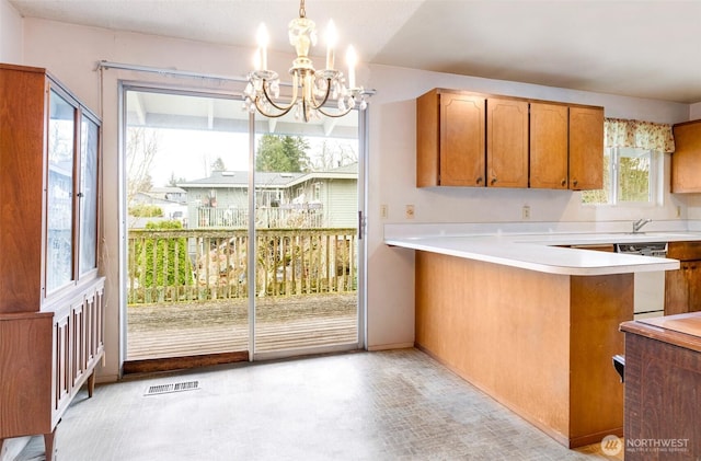 kitchen with visible vents, an inviting chandelier, brown cabinetry, light countertops, and dishwashing machine