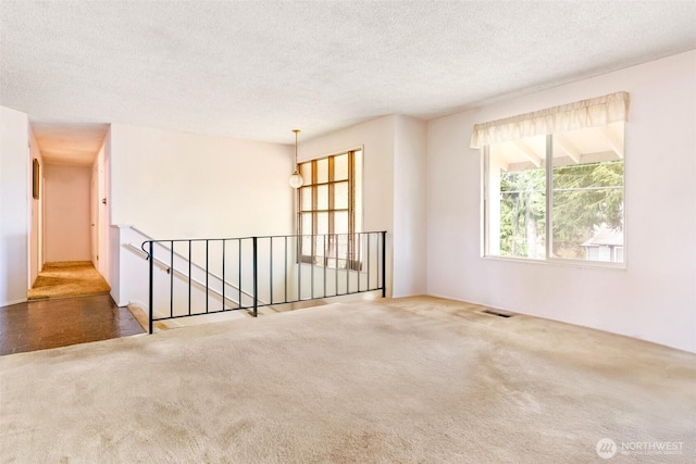 empty room featuring carpet flooring, a textured ceiling, and visible vents