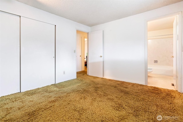 unfurnished bedroom featuring a closet, a textured ceiling, ensuite bath, and carpet floors