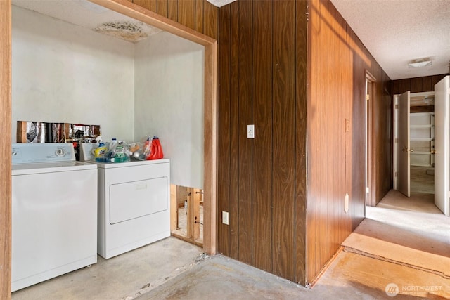 laundry area featuring a textured ceiling, wooden walls, laundry area, and washer and clothes dryer