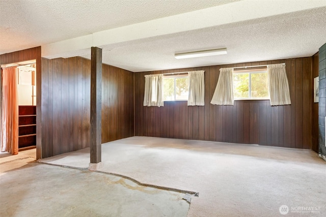 carpeted empty room with a textured ceiling, wood walls, and stairs