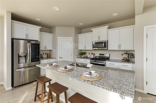 kitchen featuring appliances with stainless steel finishes, white cabinetry, sink, light stone counters, and a center island with sink