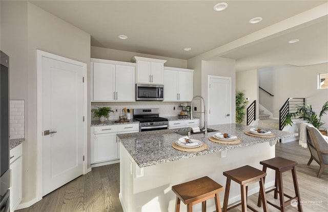 kitchen with white cabinetry, appliances with stainless steel finishes, sink, and a center island with sink