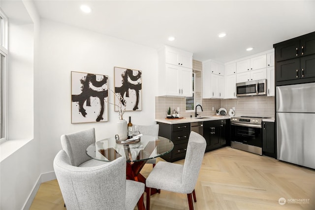 kitchen featuring sink, backsplash, stainless steel appliances, white cabinets, and light parquet flooring