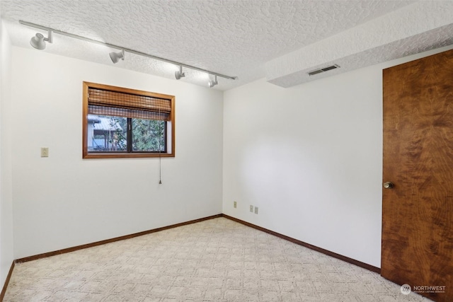 empty room featuring track lighting and a textured ceiling